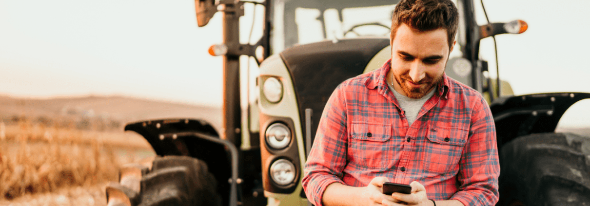Young man looking at smart phone while leaning on a tractor