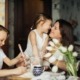 Young women rubbing noses with young child and another child sitting with them at the table