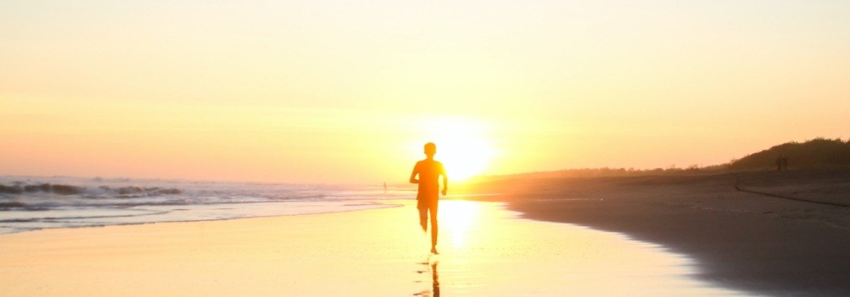 Man running on the beach with sun setting behind him