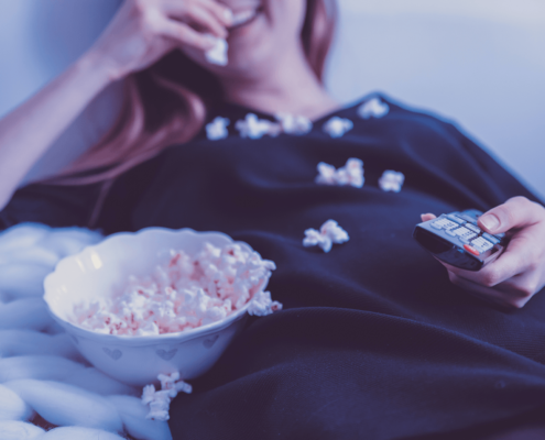 Woman lying back while eating popcorn with remote in her hand